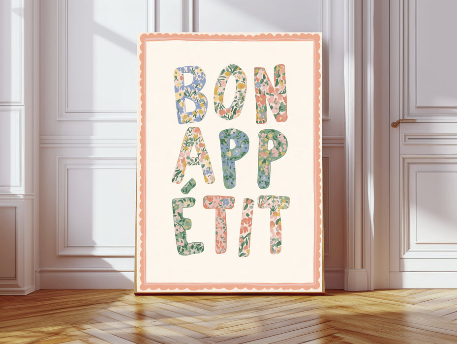 Floral Bon Appetit kitchen print with pastel flower letters and scalloped peach border, leaning against a white panelled wall