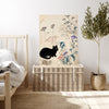 Vintage Japanese cat and owl print resting on a rattan trunk in a neutral bedroom with olive tree