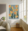Daffodil botanical art print hanging in a sunlit living room above a linen armchair with side table and plant