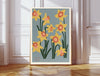 March birth flower art print of yellow daffodils on dusty blue in a gold frame, Daffodil March lettering, leaning against a panelled wall