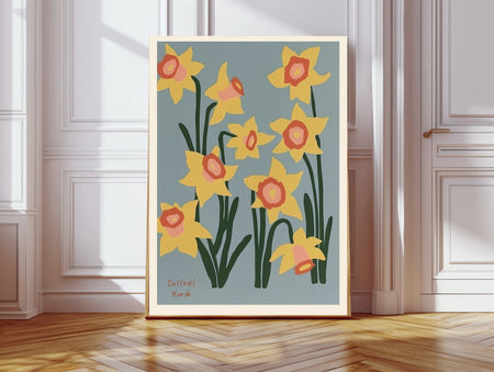 March birth flower art print of yellow daffodils on dusty blue in a gold frame, Daffodil March lettering, leaning against a panelled wall