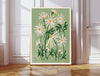 Daisy April birth flower print resting on a wicker chest beside a bed and olive tree in a neutral bedroom