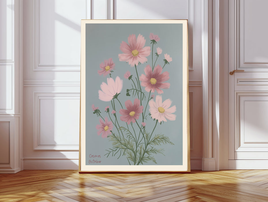 October birth flower art print of pink cosmos flowers on dusty blue in a gold frame, Cosmos October lettering, leaning against a panelled wall