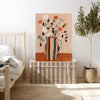 Flower vase art print resting on a wicker chest beside a bed and olive tree in a bright neutral bedroom