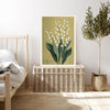 Lily of the valley birth month flower print resting on a wicker chest beside a bed and olive tree in a neutral bedroom