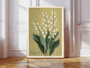 May birth flower art print of lily of the valley on olive green in a gold frame, Lily of the Valley May lettering, leaning against a panelled wall