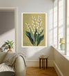 Lily of the valley May birth flower print hanging in a sunlit living room above a linen armchair with side table and plant
