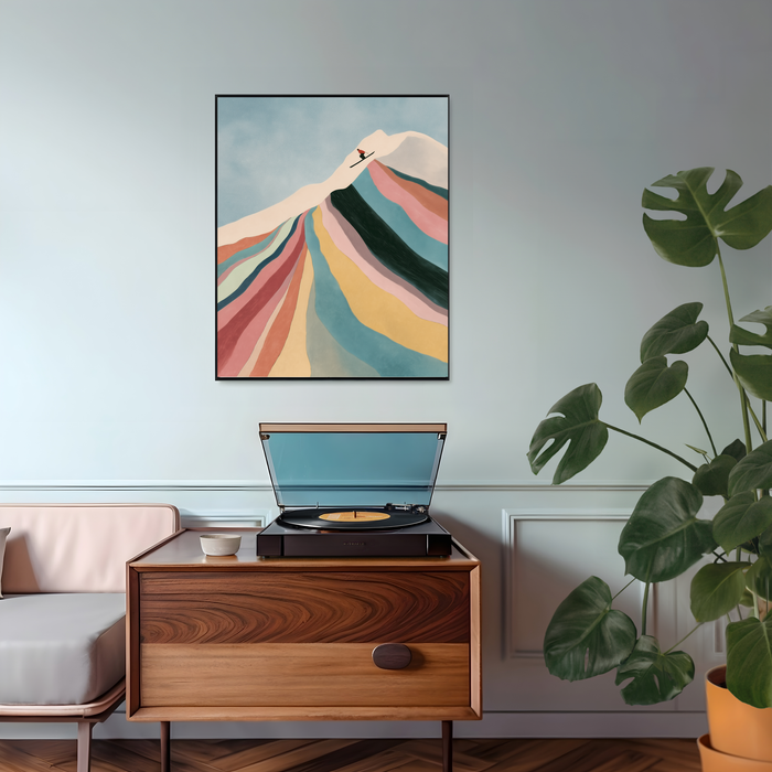 Abstract ski print with a lone skier on a cream summit above a mountainside of coral, teal and mustard ribbons, framed in black above a mid century sideboard