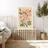 Pink rose birth month flower print resting on a wicker chest beside a bed and olive tree in a neutral bedroom