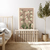 Snowdrop birth month flower print resting on a wicker chest beside a bed and olive tree in a neutral bedroom