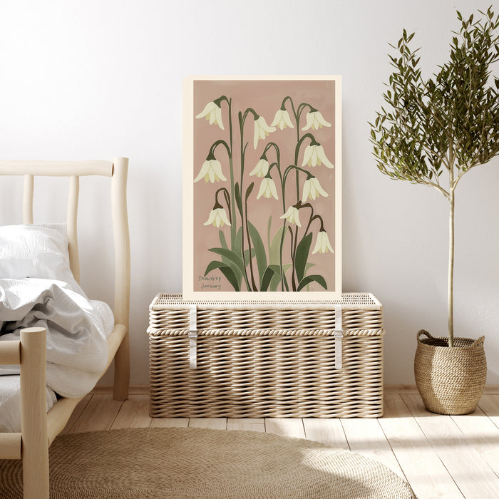 Snowdrop birth month flower print resting on a wicker chest beside a bed and olive tree in a neutral bedroom