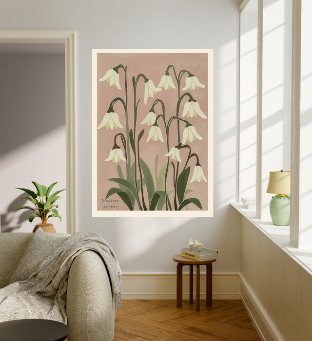 White snowdrop botanical art print hanging in a sunlit living room above a linen armchair with side table and plant